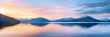 © Viktor - A vast expanse of water lies before a towering mountain range in the backdrop Clouds populate the distant sky