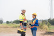 © amorn - Male and female engineer at windmill field farm, wearing safety uniform and working and inspecting quality of wind turbines