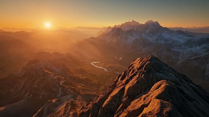 Flat lay of a mountain summit at sunset, with the sun casting a warm glow over the peaks and the valley below covered in shadow.