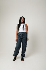 Full length portrait of young dark-skinned woman with long dark braids and posing indoor. Vertical.