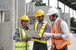 © Supachai - Team of construction engineers wearing vest and helmet safety discussing project at construction site. Group Indian foreman with laptop, paperwork working at factory making precast concrete wall.