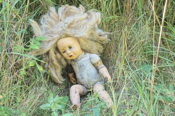 one gray dirty old doll toy lies on the ground and in the green grass on the street