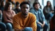 © Adi - Sad anxiety depressed black man at support group meeting for mental health and addiction issues in anonymous community space with many people around