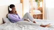 © Prostock-studio - Music Application. African American Girl In Headphones Listening To Song Sitting In Bed At Home.