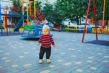 Wall Mural - A fair-haired one-year-old boy in jeans and sneakers walks on the playground. The child develops and plays in the fresh air.