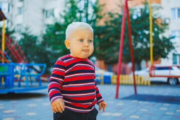 Wall Mural - A fair-haired one-year-old boy in jeans and sneakers walks on the playground. The child develops and plays in the fresh air.