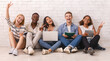 © Prostock-studio - Group of happy multiracial students studying for university exams, cheerfully gesturing at camera, white brick wall background