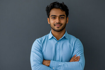 a handsome Indian man standing with his arms crossed over a grey background.