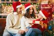 © Prostock-studio - Beautiful smiling parents in santa hats giving xmas gift to their daughter, celebrating Christmas at home, copy space