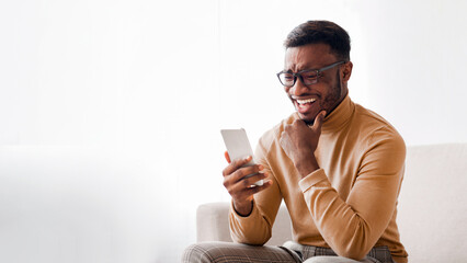 Aufkleber - Happy African American Guy Using Smatphone Chatting In Social Media Or Reading News Sitting On Sofa At Home. Selective Focus
