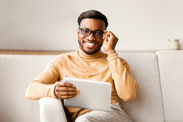 Aufkleber - Millennial Black Guy Holding Digital Tablet Smiling Looking At Camera Sitting On Sofa Indoor. Selective Focus