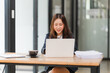 © Wicitr - Focused Asian Businesswoman: A young Asian woman in a professional setting, fully engaged in her work on a laptop, embodying focus and productivity.