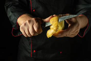 Wall Mural - Peeling potatoes with a knife. A chef prepares potatoes for mashing in a hotel or restaurant kitchen. Low key concept for cooking a vegetable dish