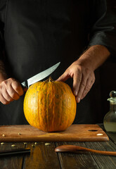 Wall Mural - Chef tries to cut ripe pumpkin on cutting board with knife. Fruit diet concept in restaurant kitchen. American national cuisine or making pie