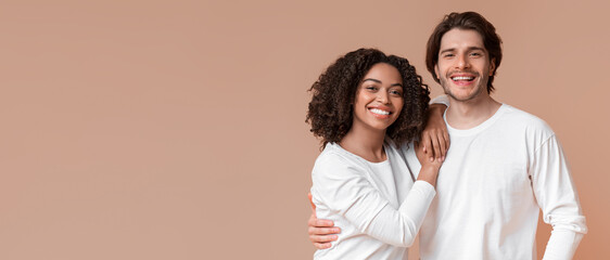 Portrait of romantic multiracial couple embracing, posing together and smiling at camera, standing over yellow background