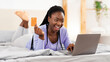 © Prostock-studio - Afro Girl Shopping Online Using Laptop And Credit Card Buying Things On Internet Lying In Bed At Home. Selective Focus