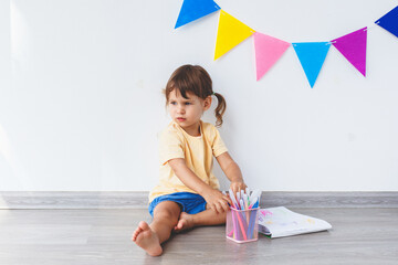 one white girl 2 years old sits in the room on the floor and draws with felt-tip pens