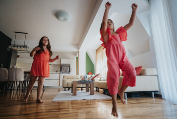 Wall Mural - Two cheerful girls playfully dancing in a spacious and brightly lit living room, expressing joy and energy. The modern home interior adds warmth and comfort to the scene.