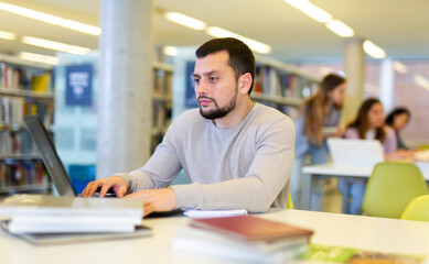 Canvas Print - European guy student, studying at the university, studies in the library on a laptop while preparing for the exam