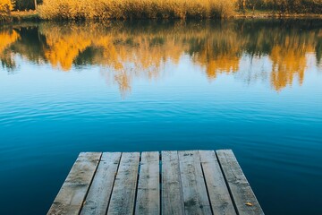 Wooden dock extending over tranquil blue lake water, reflecting fall foliage on opposite shore