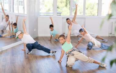 Dynamic young girl training breakdance during workout session with group of children in modern studio