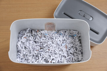 Wall Mural - Shredder and basket with paper strips on wooden table, top view