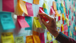 © INT888 - A hand is sorting through colorful post it notes on wall, showcasing creativity and organization.