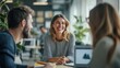 © Oulaphone - A cheerful woman engages in conversation with two colleagues in a modern office setting, surrounded by greenery and bright natural light.