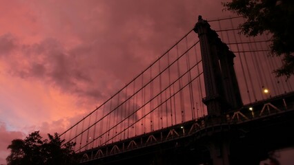 Manhattan Bridge to Brooklyn Dumbo. New York City symbol, USA travel destination. Architecture of United States of America, tourist landmark. Cables, evening sunset dramatic cloudy pink rainy sky.