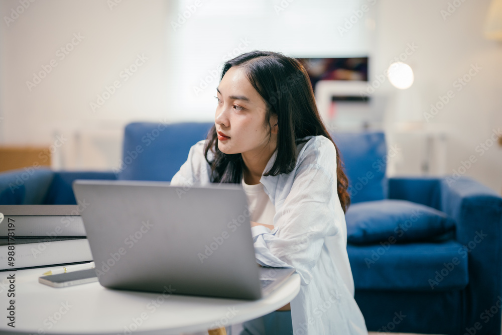 Young asian woman is sitting on the floor in her living room, working ...