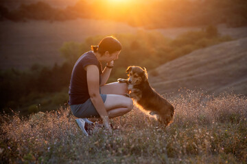 Young woman with her dog playing in the sunset