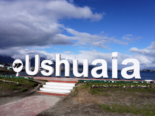  Large “Ushuaia” sign , set against a backdrop of blue sky, white clouds, and distant mountains