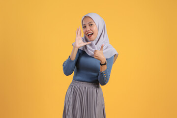 Wall Mural - asian indonesian muslim woman shouting and giving thumb up finger gesture on isolated yellow bakcground