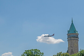 Clock tower in Luxembourg, passenger plane in blue and cloudy sky. Holiday and travel concept.