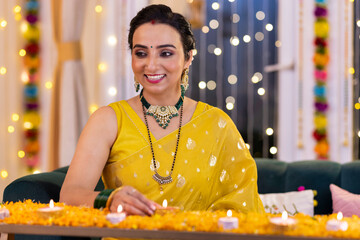 Portrait of beautiful young woman holding plate with diyas while standing in illuminated home during Diwali celebration