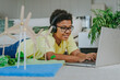 © Westend61 - Happy boy wearing wireless headphones and using laptop near solar energy school project in living room at home