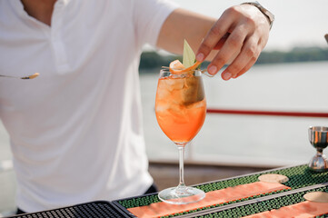 Wall Mural - Refreshing Summer Cocktail Preparation by a Bartender on a Scenic Deck with Vibrant Ingredients