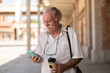 © Westend61 - Senior man holding coffee cup and using mobile phone near building
