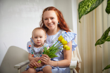 a woman with long red hair and a young girl in matching blue striped dresses with colorful tassels. 