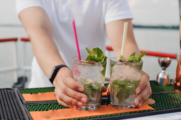 Wall Mural - Refreshing Cubes of Mojito Cocktails Served by Bartender on Scenic Waterfront