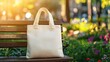 © Ganesha88 - Tote bag mockup concept image with a blank tote bag sitting outside in a park on sunny day for the large sturdy cloth unfastened bag with parallel handles with copy space