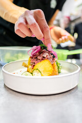 Wall Mural - A chef’s hand garnishing a colorful plated dish with fresh herbs, highlighting the final touch in meal preparation. Close-up, culinary, food presentation, professional kitchen.