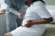 © pressmaster - Nurse using stethoscope for check-up on expectant mother sitting in clinic room. Environment is calm and clinical with focus on maternal health and professional care