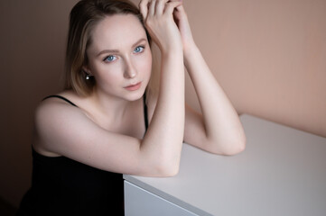 Graceful young woman in a black top posing against beige wall.