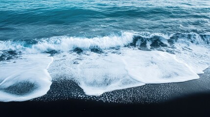 Wall Mural - Dark black sand meets the vibrant blue waves of the ocean, with soft white seafoam creating a perfect balance.