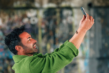 Wall Mural - young brunette caucasian man on the street outdoors taking photo or selfie with mobile phone