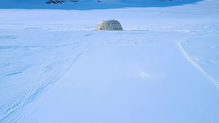 Poster - Geodesic dome stands proudly in a snowy landscape. Creating trails in the glistening powder with majestic mountains in the background
