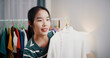 © Johnstocker - Portrait of Cheerful woman influencer is live streaming to sell clothes and measuring the sizes of clothes for customers who inquired on social media in home studio. Remote buying.