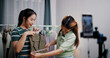 © Johnstocker - Portrait of Two cheerful woman influencers are live streaming to sell clothes and measuring the sizes of clothes for customers who inquired on social media in home studio. Remote buying.