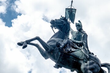 Statue of a man on a rearing horse against a cloudy sky.